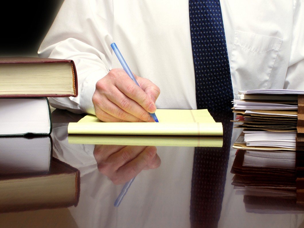 man in white shirt and blue tie writing in legal pad